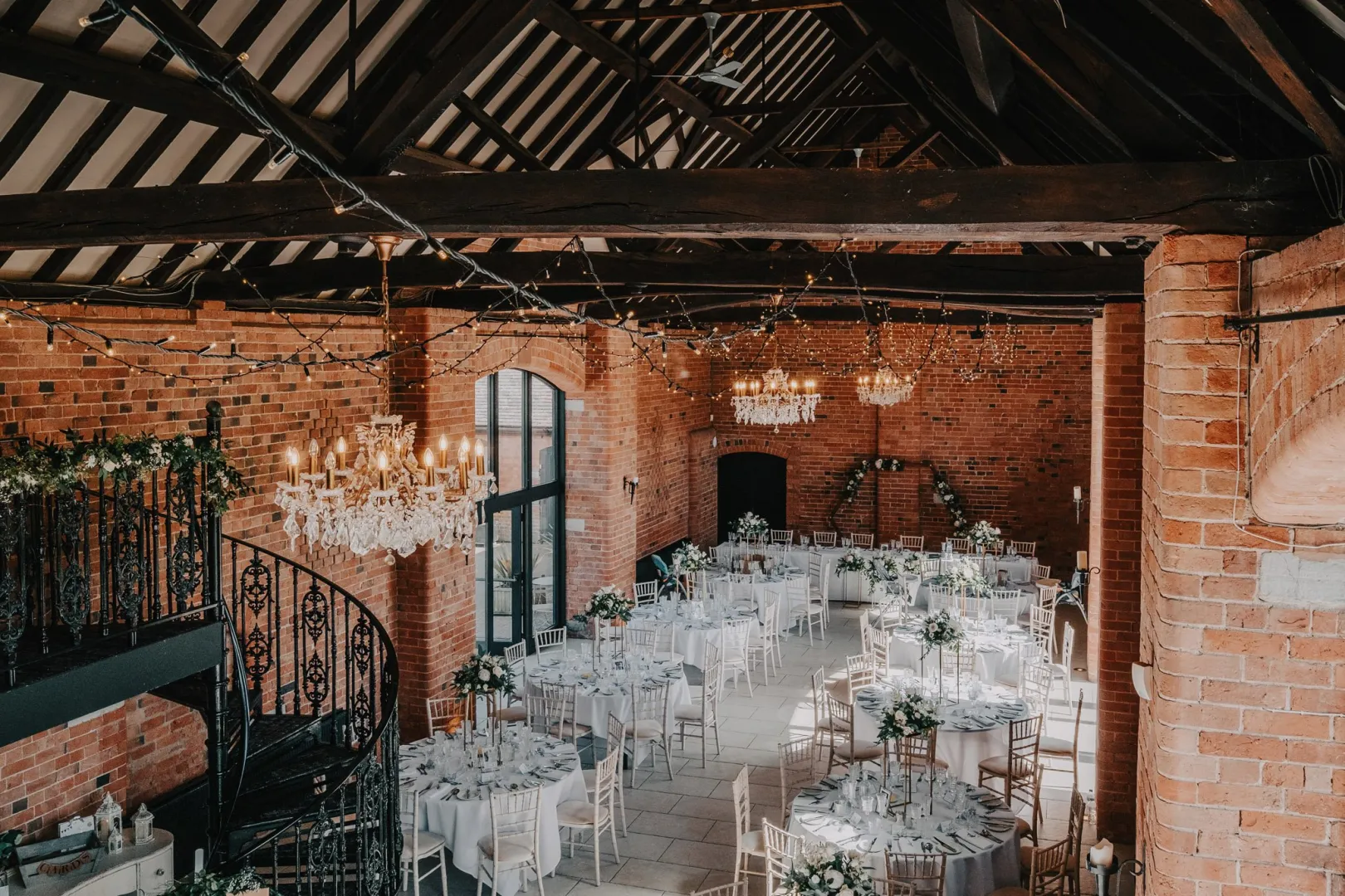 Stylish rustic venue showcasing exposed brick walls, elegant chandeliers, and round tables set for a wedding reception.