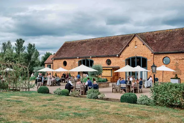 Charming rustic barn with outdoor patio, guests under umbrellas, and lush greenery, perfect for a relaxed wedding celebration.