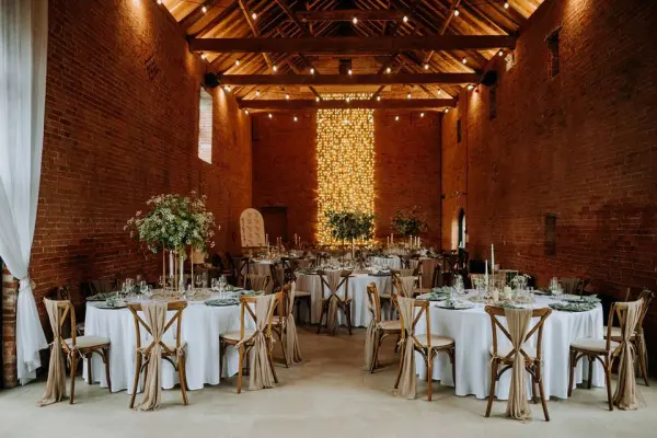 Rustic barn venue featuring wooden beams, elegant round tables, and lush floral centerpieces, illuminated by soft, warm lighting.