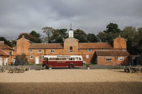 Charming rustic venue with a vintage bus, sandy courtyard, and brick buildings surrounded by trees, perfect for outdoor celebrations.