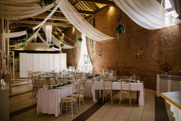 Warm rustic barn interior featuring draped fabric, intimate tables, and elegant decor, perfect for a cozy wedding reception.