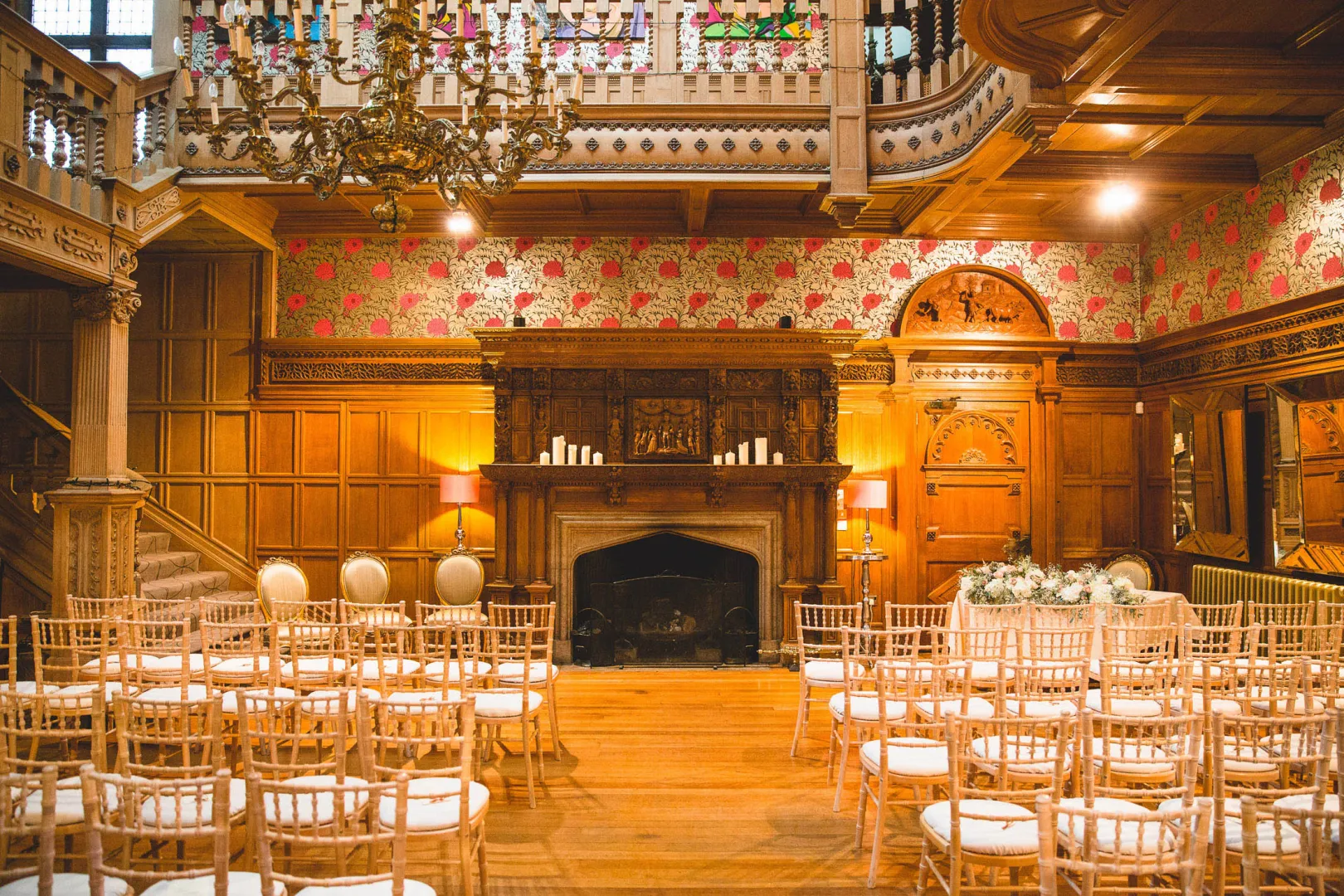 Elegant indoor ceremony space featuring wooden paneling, a grand fireplace, and rows of chiavari chairs under a decorative chandelier.