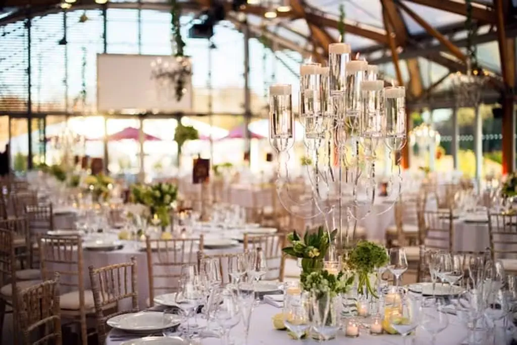 Elegant dining setup featuring crystal chandeliers, lush floral centerpieces, and a sunlit venue with stunning glass architecture.