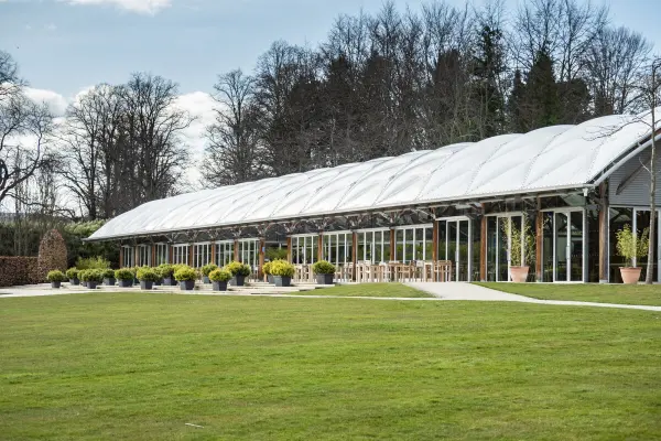 Spacious venue featuring a modern glass-walled structure, surrounded by manicured lawns and lush greenery, perfect for any wedding celebration.