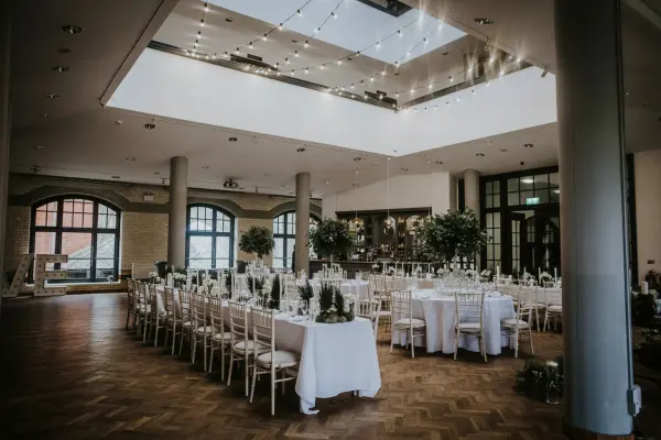 Spacious indoor wedding venue featuring elegant tables, lush greenery, and stunning natural light from the skylight above.