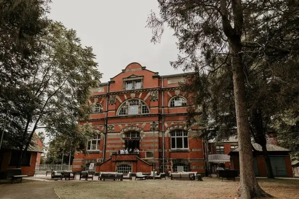 Historic brick venue surrounded by lush greenery, featuring large windows and an elegant outdoor terrace perfect for weddings.
