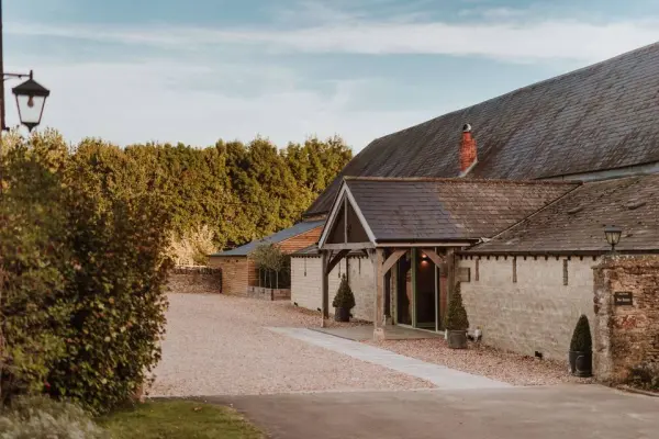Charming rustic barn with gravel path, framed by lush greenery, ideal for a cozy yet elegant wedding celebration.
