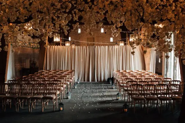 Charming indoor ceremony space adorned with elegant floral accents, rows of classic wooden chairs, and soft draped curtains.