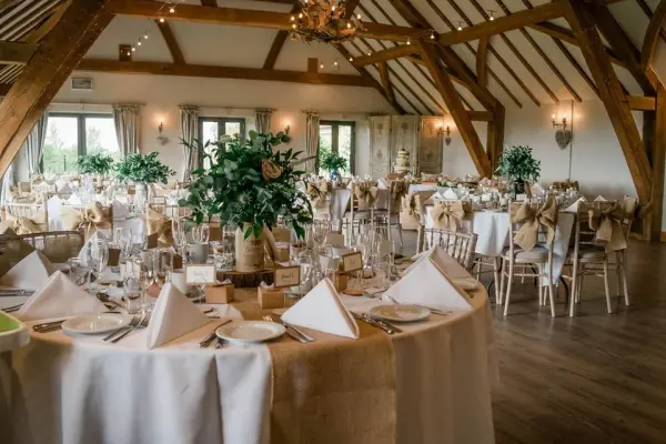 Elegant reception space featuring rustic wooden beams, round tables adorned with floral arrangements, and soft lighting for a romantic ambiance.