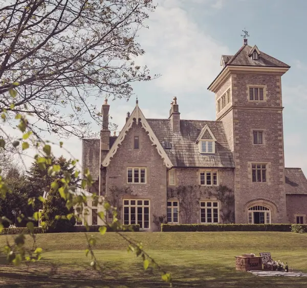 A stunning stone mansion with a tower, surrounded by lush lawns and trees, offering a picturesque setting for elegant outdoor ceremonies.