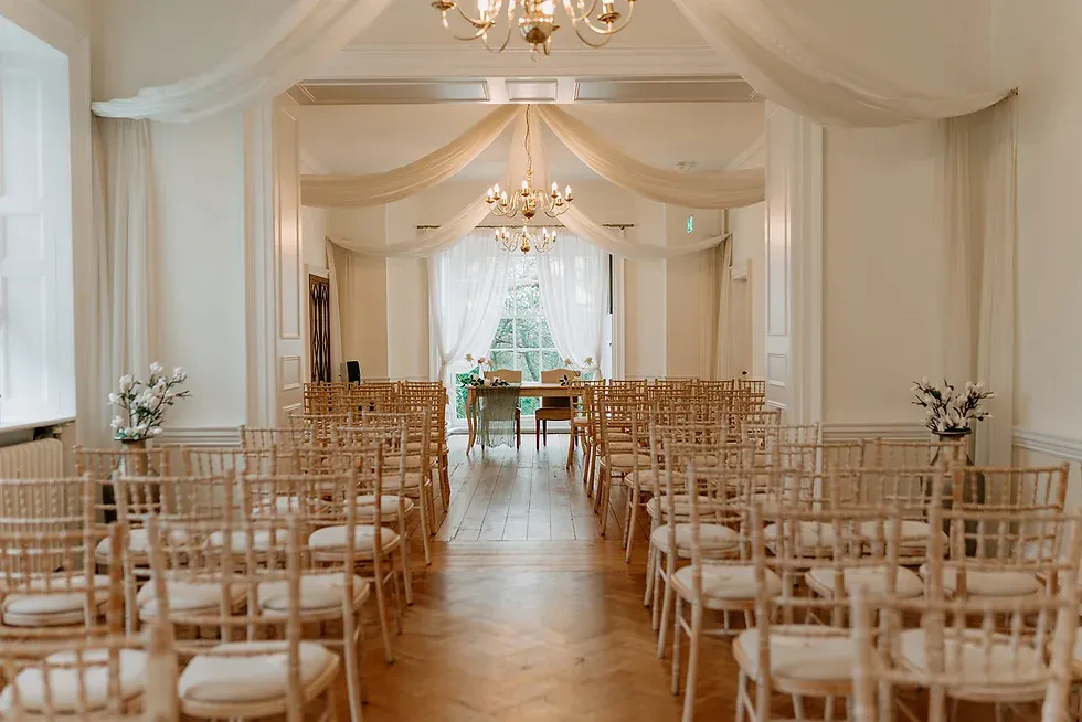 Bright ceremony space with elegant chandeliers, draped ceilings, and rows of wooden chairs, creating a romantic, intimate atmosphere.