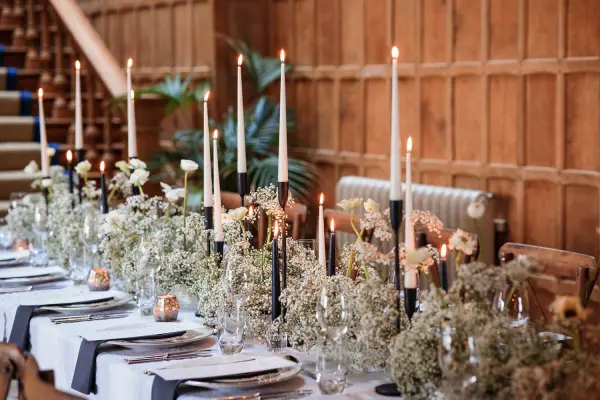 Elegant wedding reception table adorned with soft greenery, candles, and delicate floral arrangements, set against rich wooden paneling.