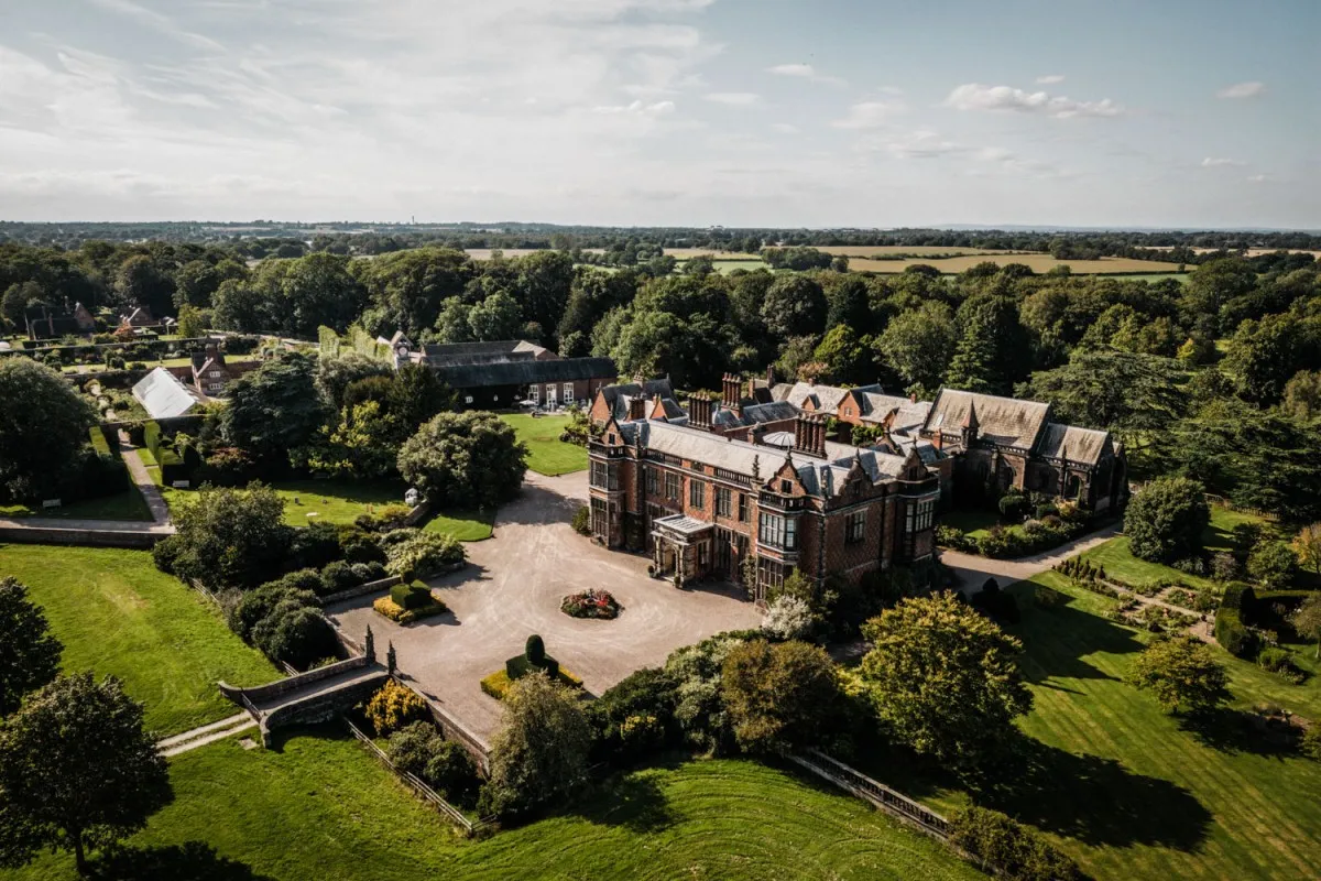 Aerial view of a grand manor surrounded by lush gardens, perfect for outdoor ceremonies and picturesque celebrations.