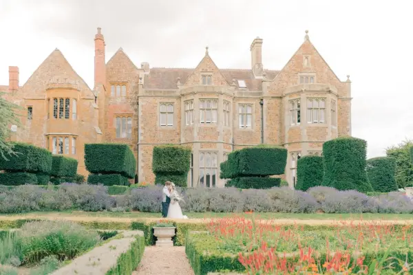 Charming historic manor set amidst lush gardens, featuring manicured hedges and vibrant flower beds, perfect for outdoor ceremonies.