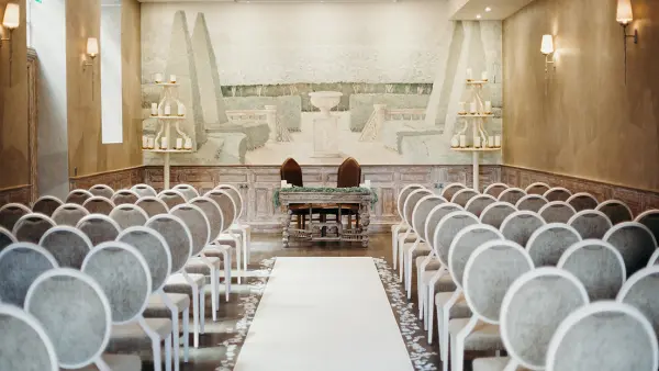 Elegant ceremony space featuring soft, circular chairs, a striking mural backdrop, and a center aisle leading to a decorative altar.