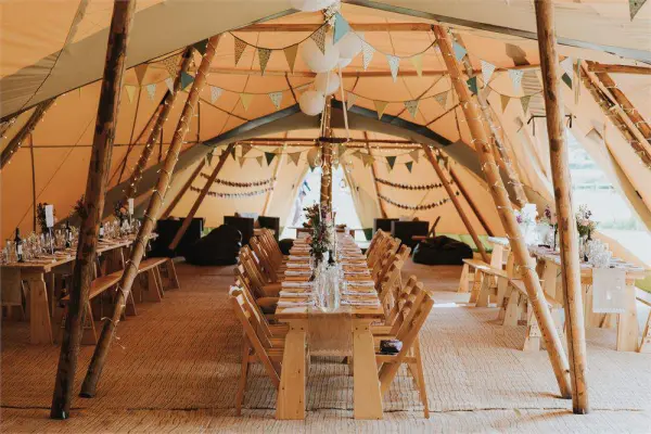 Charming tent wedding venue featuring rustic wooden tables, string lights, and bunting, creating a cozy, inviting atmosphere for celebrations.