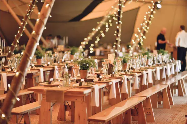 A cozy, bohemian reception space featuring long wooden tables adorned with greenery and fairy lights, creating an inviting atmosphere.