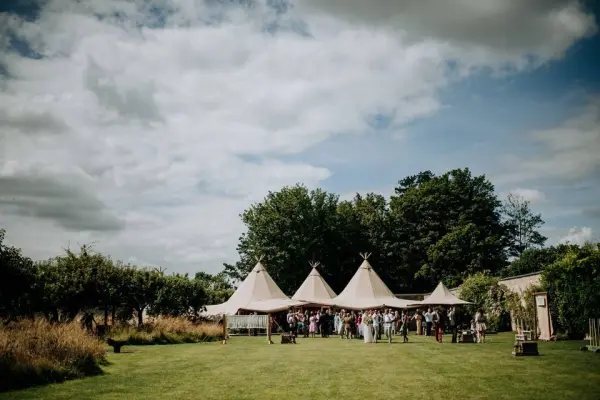 A spacious outdoor ceremony area featuring elegant tipis, surrounded by lush greenery and a vibrant reception atmosphere.