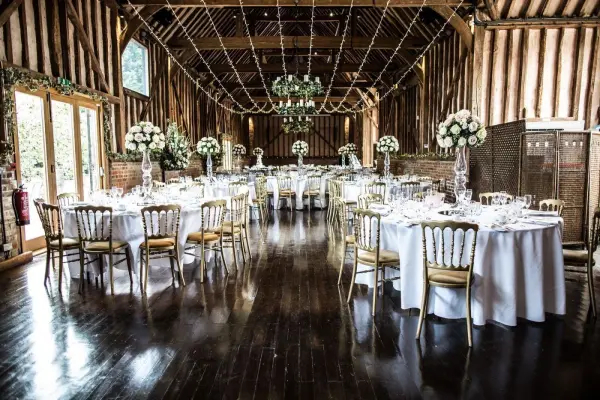 Elegant rustic barn with dark hardwood floors, adorned with floral centerpieces and sparkling chandeliers, ideal for intimate receptions.