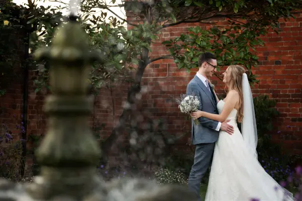 A couple shares a romantic moment by a classic fountain, surrounded by lush greenery and rustic brick walls, perfect for intimate weddings.