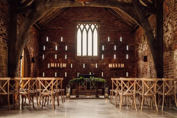 Charming rustic venue with exposed brick walls, wooden beams, and arranged chairs for an intimate ceremony under a large window.