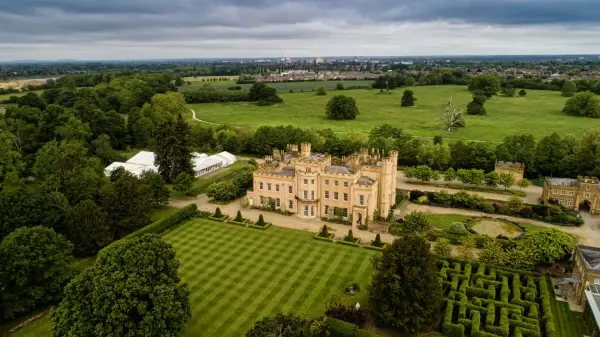Aerial view of a charming mansion surrounded by manicured lawns, lush gardens, and expansive green fields, perfect for elegant outdoor weddings.