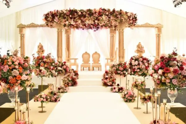 Lush floral arrangements line the aisle, leading to an elegant altar adorned with draped fabric and a flower-covered canopy.
