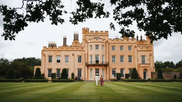 Stunning stately mansion with vibrant orange facade, expansive manicured lawn, and romantic outdoor space, perfect for wedding ceremonies.