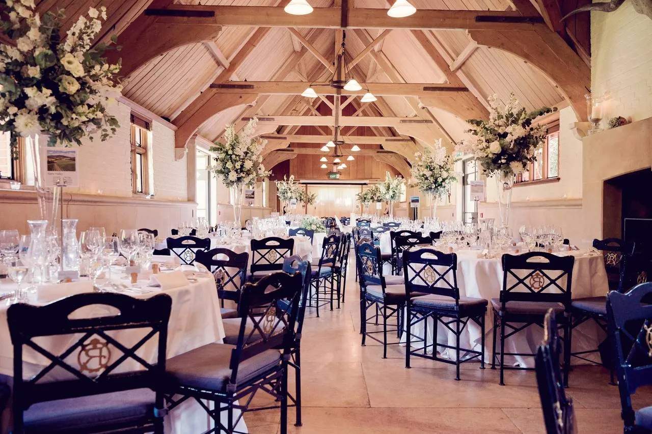 Elegant reception space featuring rustic wooden beams, beautifully set tables, and lush floral arrangements, perfect for a wedding celebration.