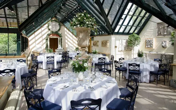 Elegant greenhouse venue with sun-drenched tables, plush floral centerpieces, and a charming, romantic atmosphere for wedding receptions.