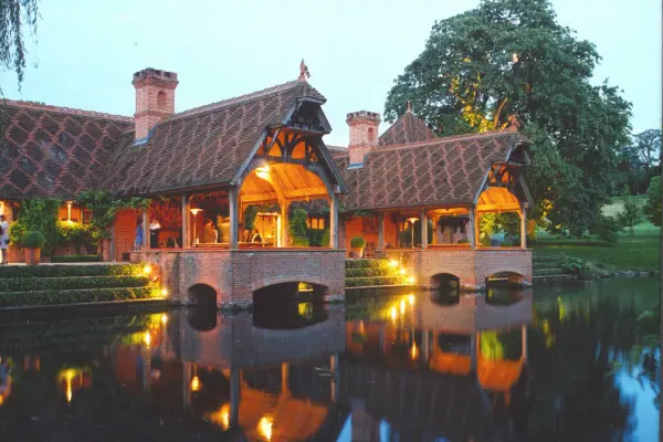 Charming venue featuring rustic pavilions with thatched roofs, softly lit by evening lights, overlooking a serene water reflection.