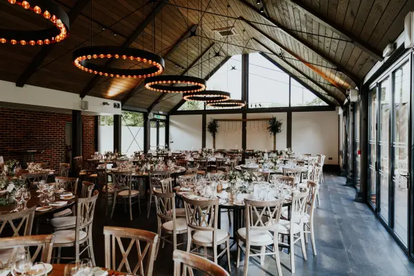 Charming reception space featuring rustic wooden beams, elegant lighting, and round tables set for a wedding celebration.