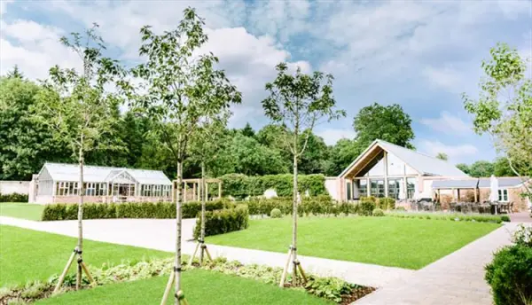 Lush green lawns and neatly arranged trees surround a contemporary venue with large windows, offering inviting outdoor spaces for weddings.