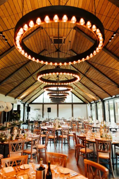 Stylish indoor reception space featuring rustic wooden beams, elegant chandeliers, and beautifully arranged tables for a wedding celebration.
