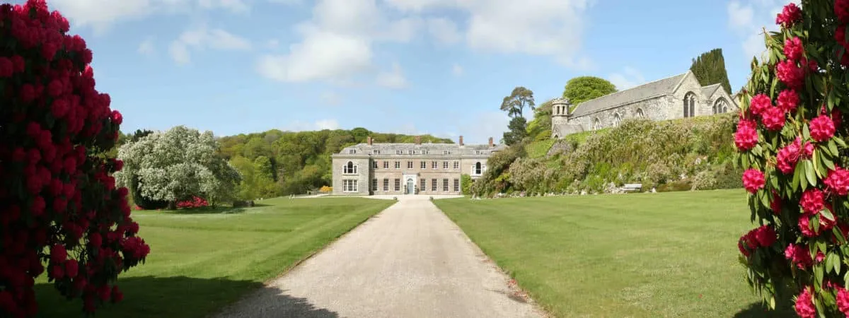 Elegant estate entrance featuring manicured lawns, vibrant floral borders, and a historic chapel in the background, ideal for picturesque weddings.