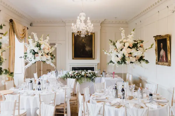 Elegant ballroom featuring round tables set with fine china, lavish floral centerpieces, and a chandelier, perfect for a sophisticated wedding.