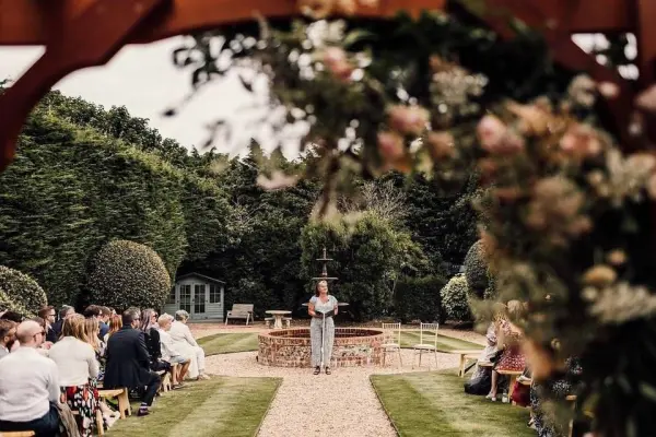 Charming outdoor ceremony space framed by lush greenery, featuring a fountain and guest seating along a gravel path.