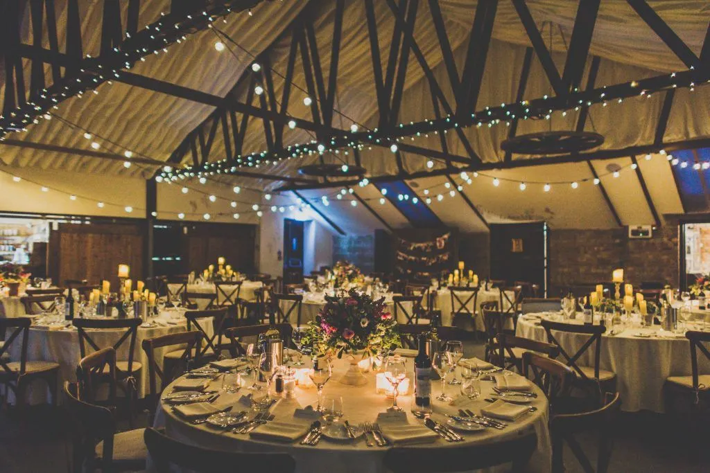 Elegant reception space featuring rustic wooden beams, twinkling string lights, and beautifully set tables for an intimate wedding celebration.