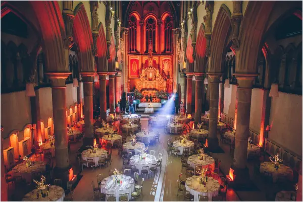 Elegant indoor wedding venue with high ceilings, ornate architecture, illuminated tables, and a stunning altar backdrop.