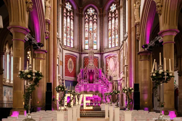 A stunning ceremony space featuring colorful stained glass, elegant floral arrangements, and illuminated "LOVE" letters under soaring arches.