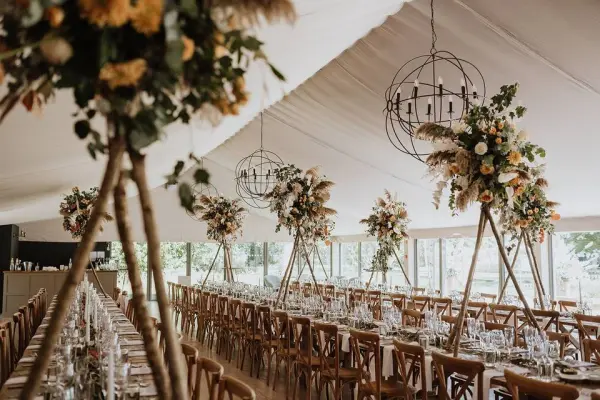 Stylish reception area featuring long wooden tables, elegant floral centerpieces, and warm pendant lighting under a tented ceiling.