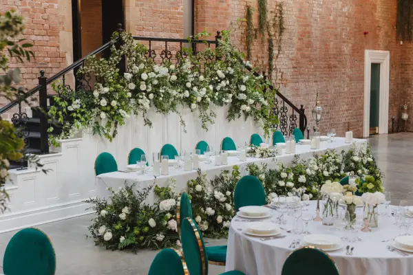 Stylish wedding reception featuring elegant tables with lush floral centerpieces and a beautiful staircase adorned with greenery and white roses.
