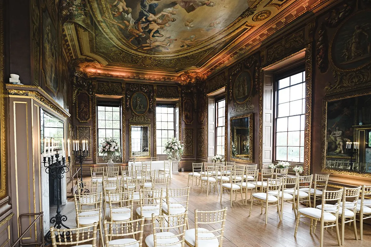 Elegant indoor ceremony space features opulent frescoed ceilings, ornate decor, and golden chiavari chairs arranged for guests.
