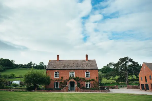 Charming red brick house set amid lush green fields, offering a picturesque backdrop for outdoor ceremonies and intimate gatherings.