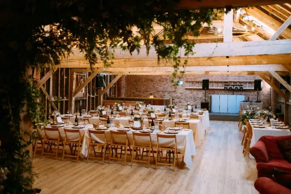 Rustic barn interior featuring long banquet tables, warm wood beams, and elegant floral centerpieces, perfect for intimate wedding gatherings.