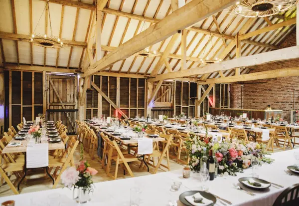 Charming rustic barn venue featuring long wooden tables set with elegant dinnerware and vibrant floral arrangements for a warm, inviting atmosphere.