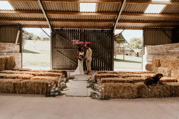 Intimate ceremony in a rustic barn, featuring straw bale seating and a charming backdrop of wooden doors and scenic outdoor views.