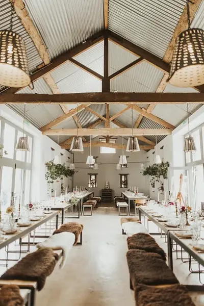 Spacious reception area featuring high ceilings, rustic wooden beams, long tables, and elegant lighting, perfect for intimate weddings.