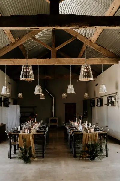 Stylish barn interior featuring rustic wooden beams, elegant long tables adorned with candles, and warm pendant lighting for a cozy ambiance.