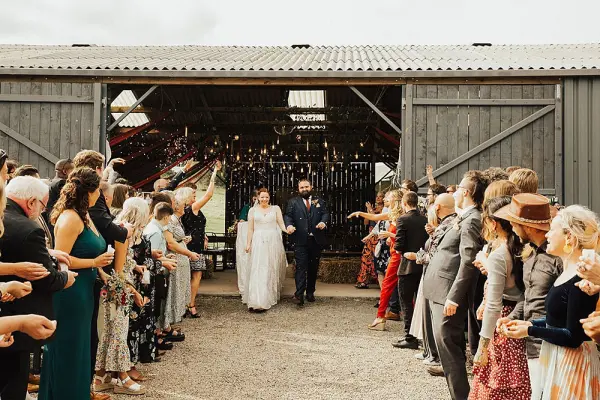 A rustic barn entrance adorned with chandeliers, framed by guests celebrating as the couple joyfully exits.